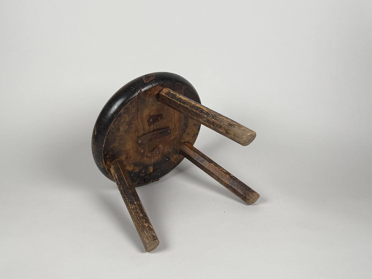 Pall med skålad sits av björk, åttkantiga ben av furu. Benen med ojämn längd så pallen lutar. Sitsen sprucken samt lagad med läderbitar och nubb. 