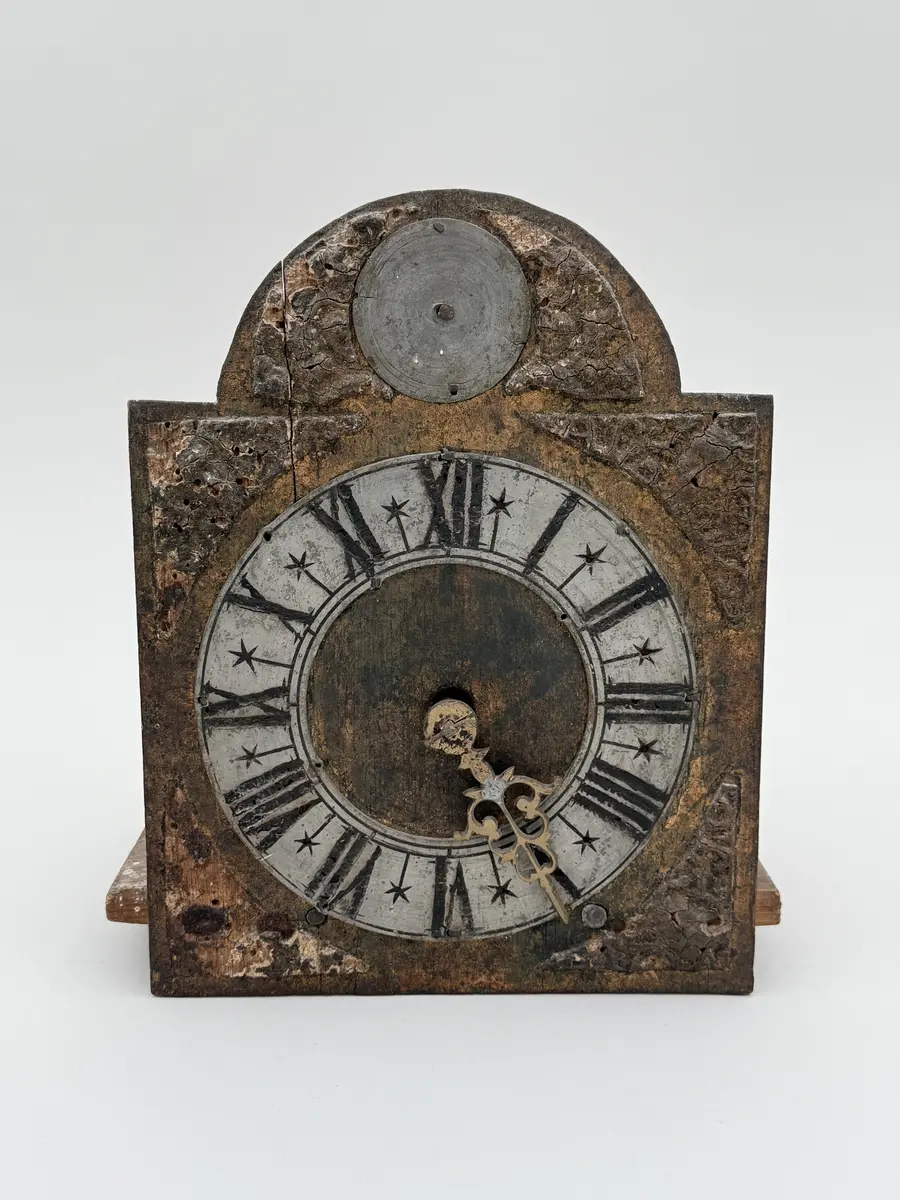 Förgylld med pastellagedekor (skadad), urtavla av bly med romerska siffror, visare av mässing, rund disk av bly ovan urtavlan. Urverket med kuggar av mässing, bottenplatta av buru som hålls p plats av mässingsbeslag. Snöre löper ner från urverket med en trissa i änden. 