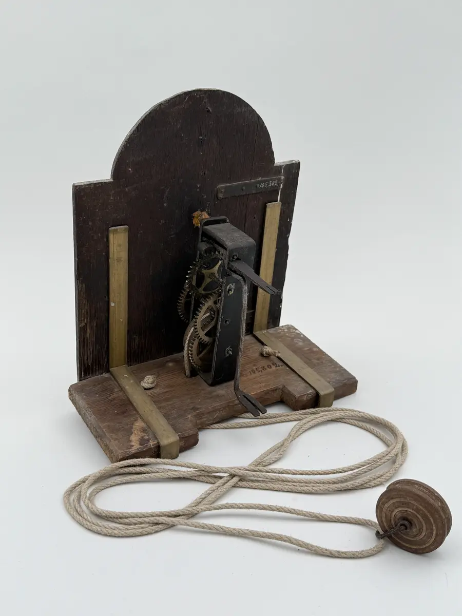 Förgylld med pastellagedekor (skadad), urtavla av bly med romerska siffror, visare av mässing, rund disk av bly ovan urtavlan. Urverket med kuggar av mässing, bottenplatta av buru som hålls p plats av mässingsbeslag. Snöre löper ner från urverket med en trissa i änden. 