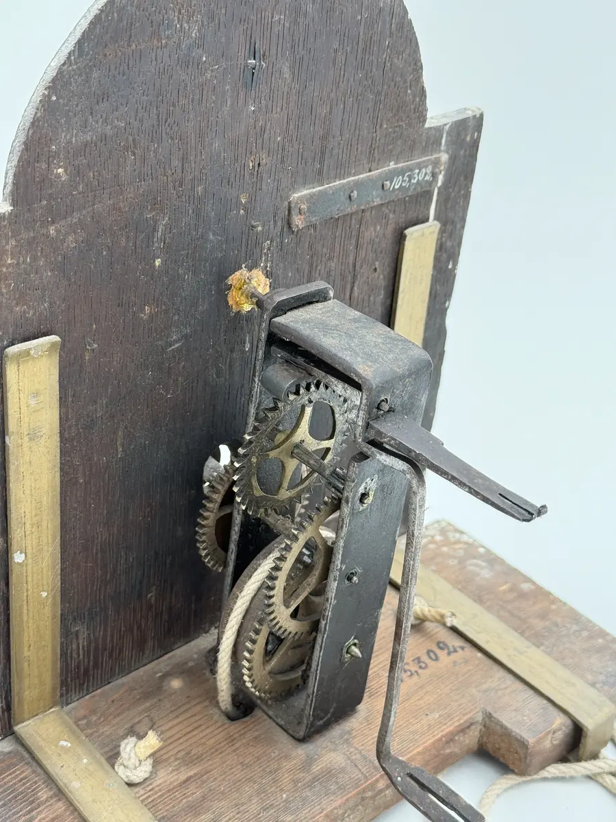 Förgylld med pastellagedekor (skadad), urtavla av bly med romerska siffror, visare av mässing, rund disk av bly ovan urtavlan. Urverket med kuggar av mässing, bottenplatta av buru som hålls p plats av mässingsbeslag. Snöre löper ner från urverket med en trissa i änden. 