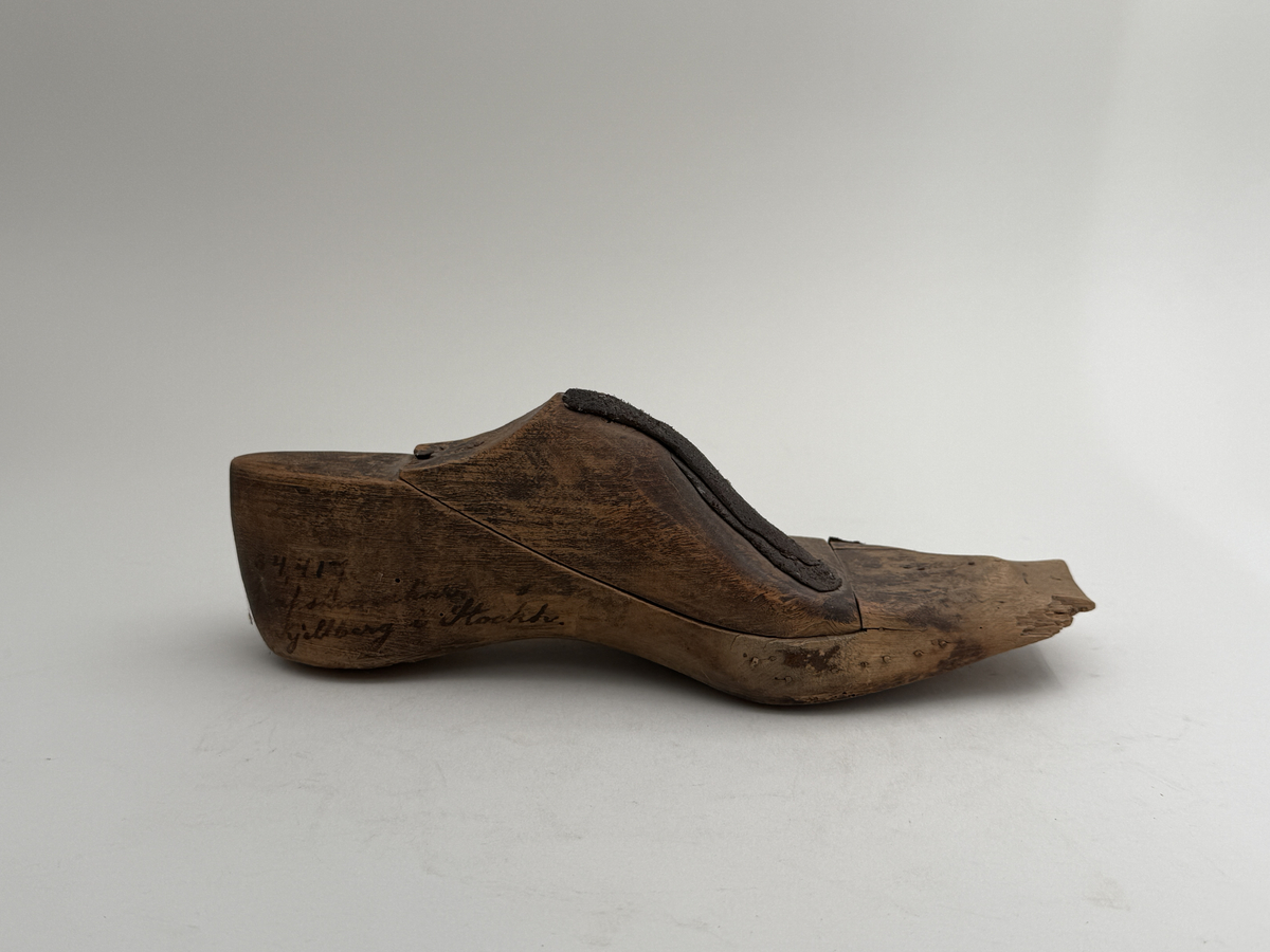 Skoläst för herrskor. Vänsterfot.
Gjord i björkträ med läderbitar fastpliggade på vristdelen. 
 