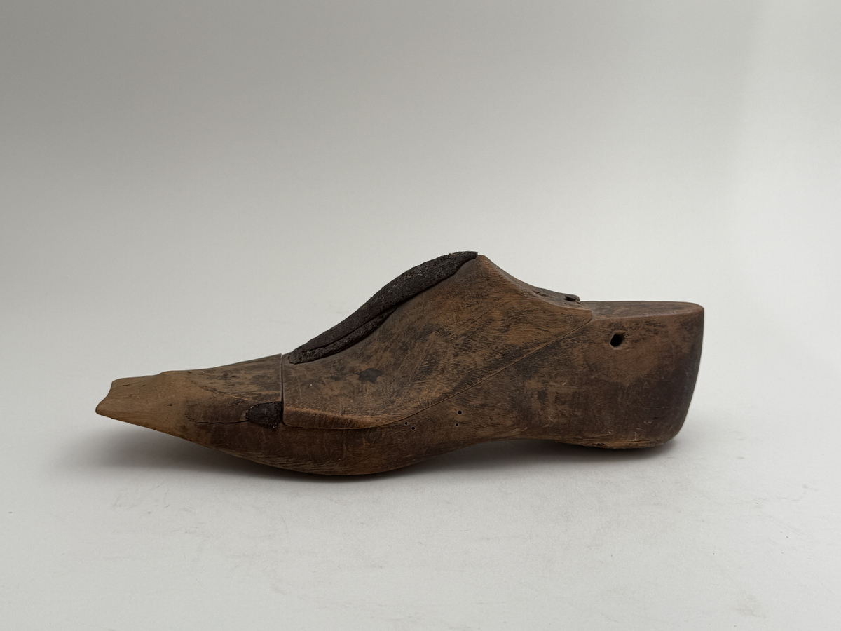 Skoläst för herrskor. Vänsterfot.
Gjord i björkträ med läderbitar fastpliggade på vristdelen. 
 