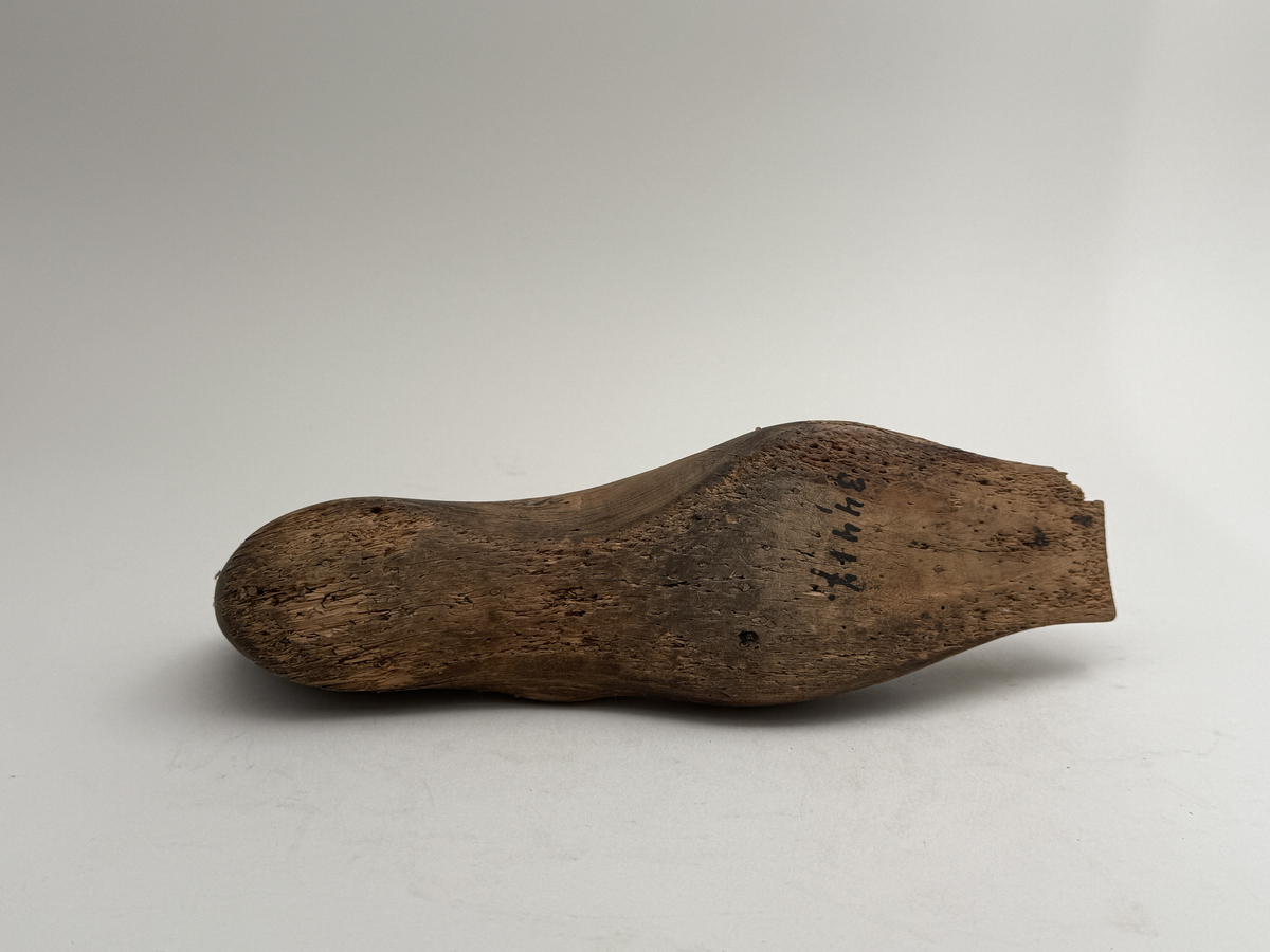 Skoläst för herrskor. Vänsterfot.
Gjord i björkträ med läderbitar fastpliggade på vristdelen. 
 