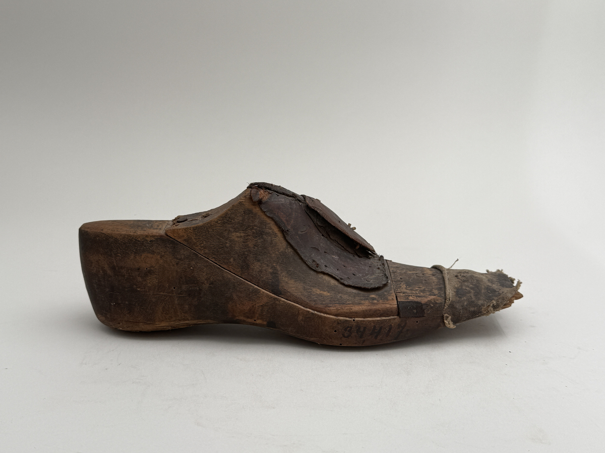 Skoläst för herrskor. Högerfot.
Gjord i björkträ med läderbitar fastpliggade på vristdelen. Tåhällen klädd med lärft. 
 