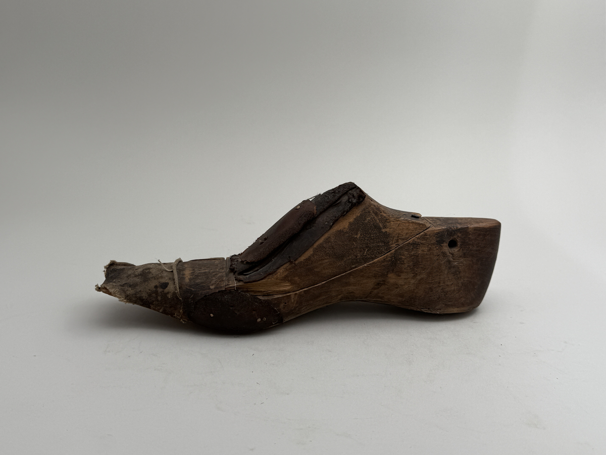 Skoläst för herrskor. Högerfot.
Gjord i björkträ med läderbitar fastpliggade på vristdelen. Tåhällen klädd med lärft. 
 