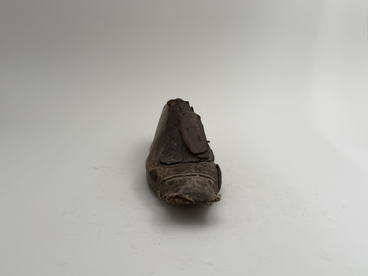 Skoläst för herrskor. Högerfot.
Gjord i björkträ med läderbitar fastpliggade på vristdelen. Tåhällen klädd med lärft. 
 