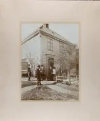 Gruppefotografi. 3 kvinner og 4 menn utenfor et trehus.