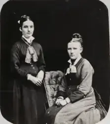 Portrett av to kvinner med oppsatt hår, den ene sittende på 