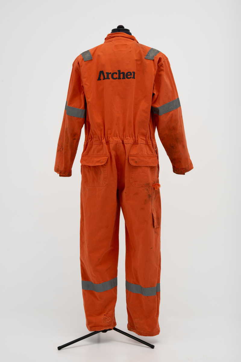 Kjeledress i størrelse 60 med Archer sin logo. Kjeledressen er utstyrt med flere utvendige lommer og reflekser. Innvendig i nakke er det festet en etikett med plattformnavn og QR-kode.