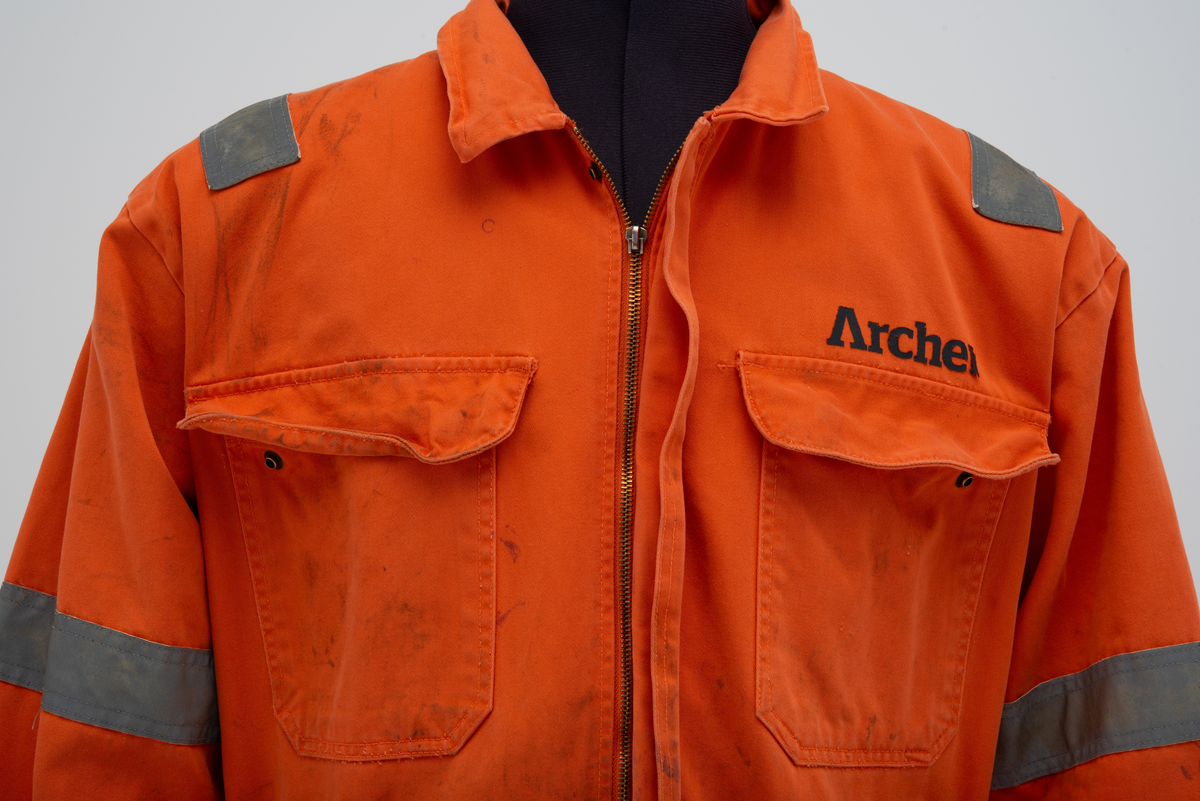 Kjeledress i størrelse 60 med Archer sin logo. Kjeledressen er utstyrt med flere utvendige lommer og reflekser. Innvendig i nakke er det festet en etikett med plattformnavn og QR-kode.