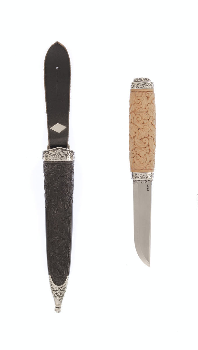 Kniv med utskore skaft og gravera holkar, på toppen ein støypt hund.
Slire av horn, utskoren på begge sider, holkar av sylv som er gravera.