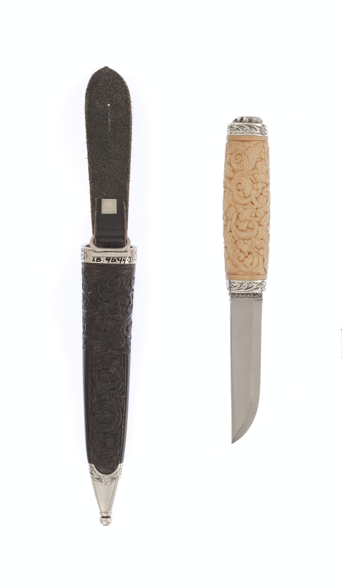 Kniv med utskore skaft og gravera holkar, på toppen ein støypt hund.
Slire av horn, utskoren på begge sider, holkar av sylv som er gravera.