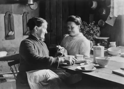 Kaffekos i bryggerhuset på Hauge, mor og datter i H. N. Haugens gate, Rolvsøy, ca. 1915.
Ellen Moum (til venstre) og datteren Helga G. Jakobsen.
