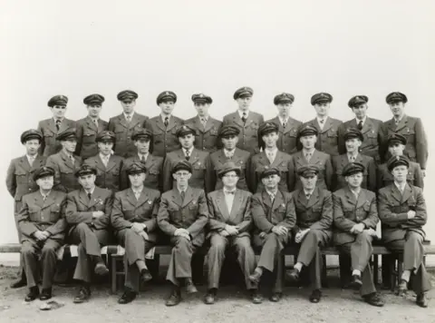 Gruppebilde av bussjåfører i uniform, med eier (disponent) i midten av første rekke. Glombuss? Alle ukjente.