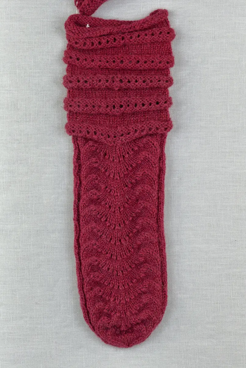 Ett par stickade tumvantar, med ränder i avigstickning och ett hålvarv mitt på varje rand på mudd/krage och vante i påfågelmönstrad spets-stickning i 2-trådigt ullgarn. Vanten har instickad tumme och toppen är formad med bandhoptagning.