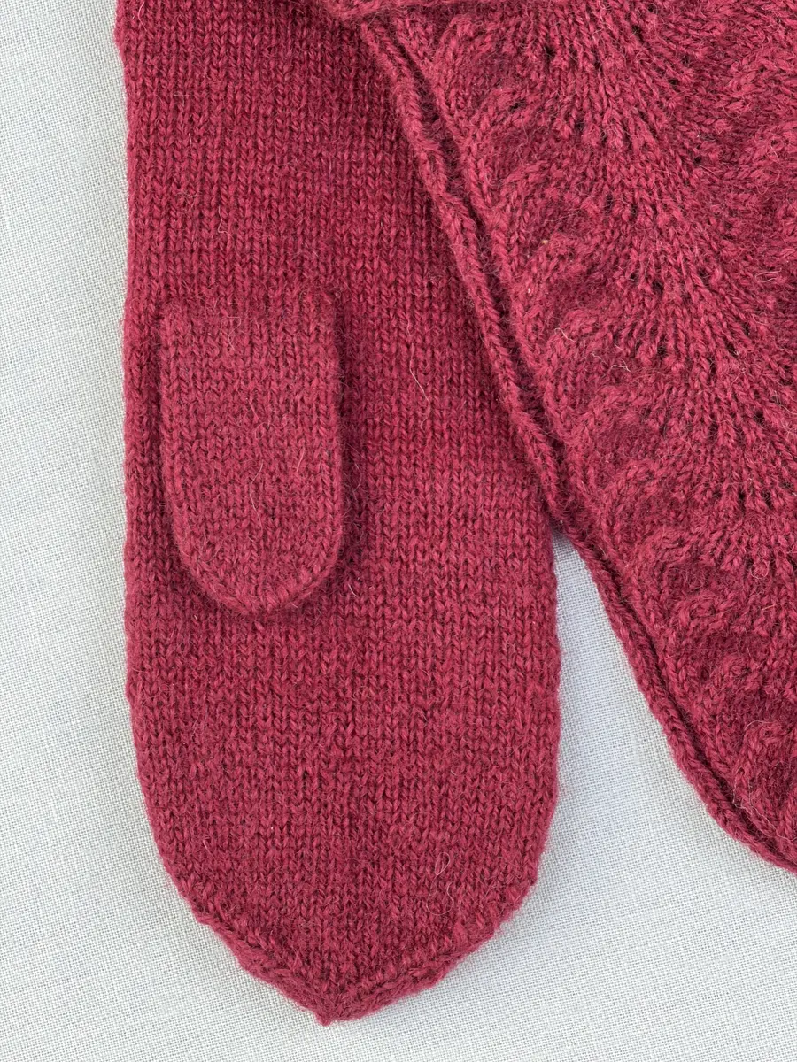 Ett par stickade tumvantar, med ränder i avigstickning och ett hålvarv mitt på varje rand på mudd/krage och vante i påfågelmönstrad spets-stickning i 2-trådigt ullgarn. Vanten har instickad tumme och toppen är formad med bandhoptagning.