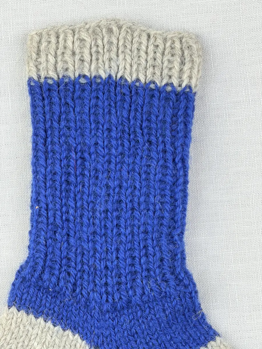 En stickad socka, med randig mudd i 1-1 resår (1 rät och 1 avig maska) och randig fot i slätstickning, av 3-trådigt Sportgarn i ull.
Gjord efter Bergå beskrivning D 315 från Bergå Färgeri & Ullspinneri, Stora Skedvi, Dalarna.