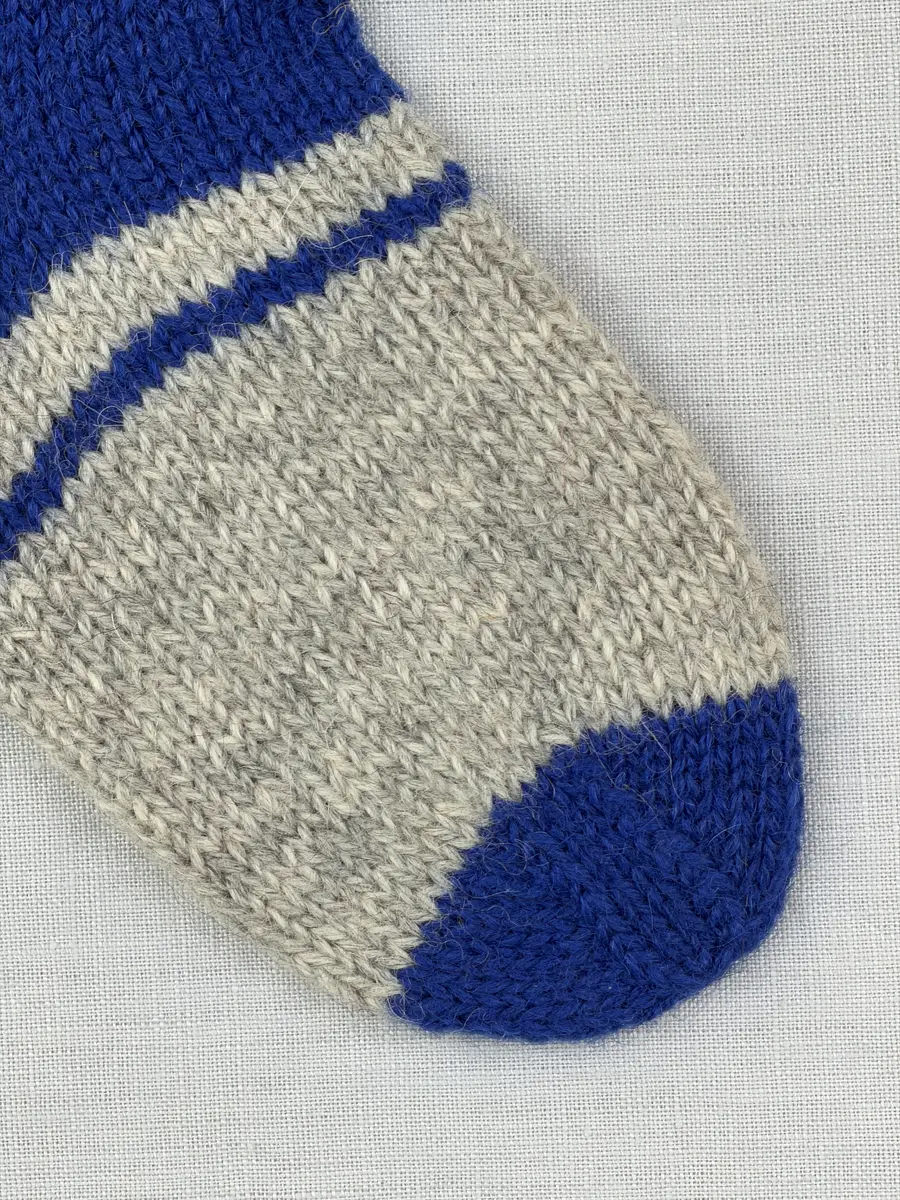 En stickad socka, med randig mudd i 1-1 resår (1 rät och 1 avig maska) och randig fot i slätstickning, av 3-trådigt Sportgarn i ull.
Gjord efter Bergå beskrivning D 315 från Bergå Färgeri & Ullspinneri, Stora Skedvi, Dalarna.