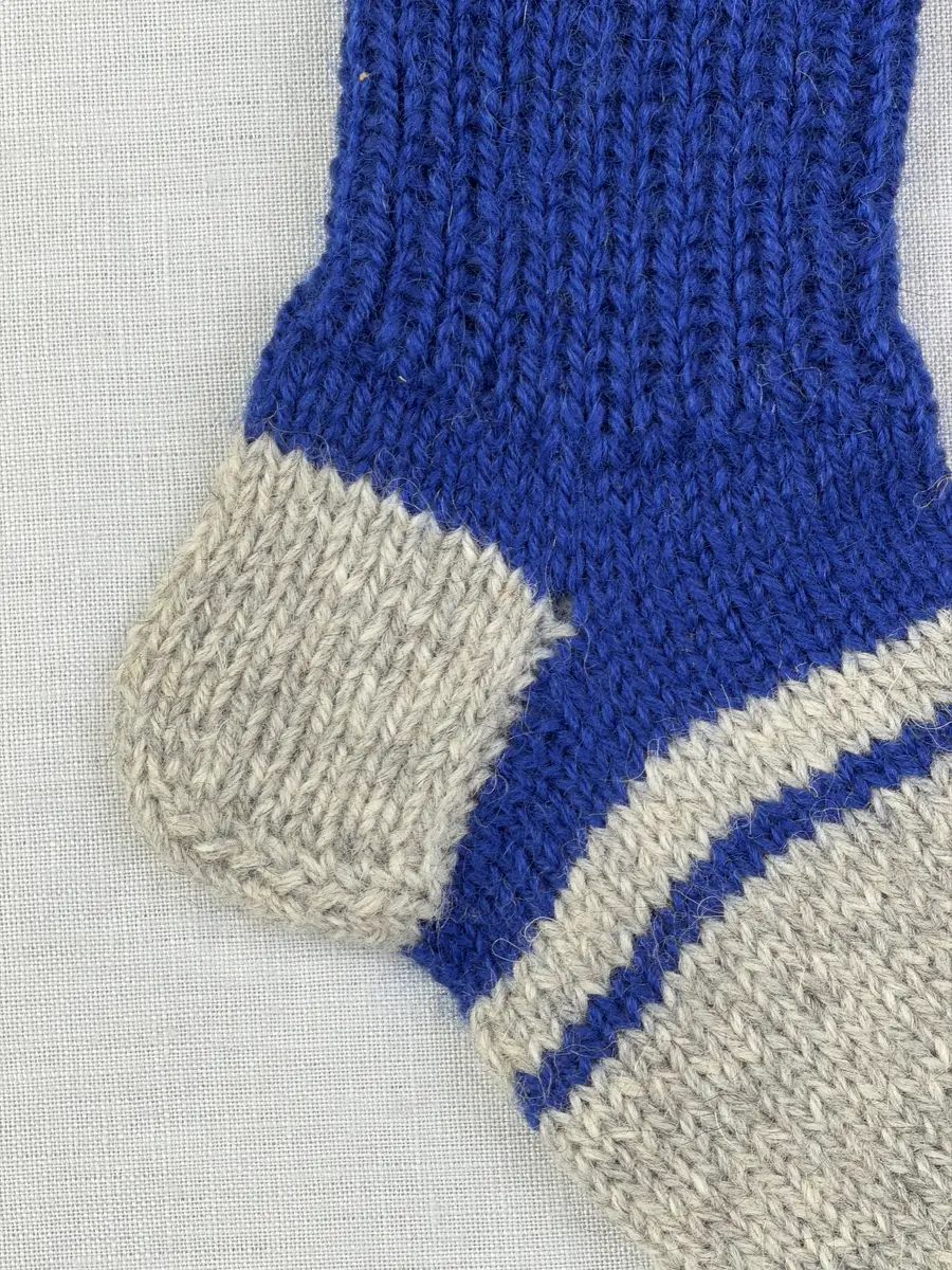 En stickad socka, med randig mudd i 1-1 resår (1 rät och 1 avig maska) och randig fot i slätstickning, av 3-trådigt Sportgarn i ull.
Gjord efter Bergå beskrivning D 315 från Bergå Färgeri & Ullspinneri, Stora Skedvi, Dalarna.