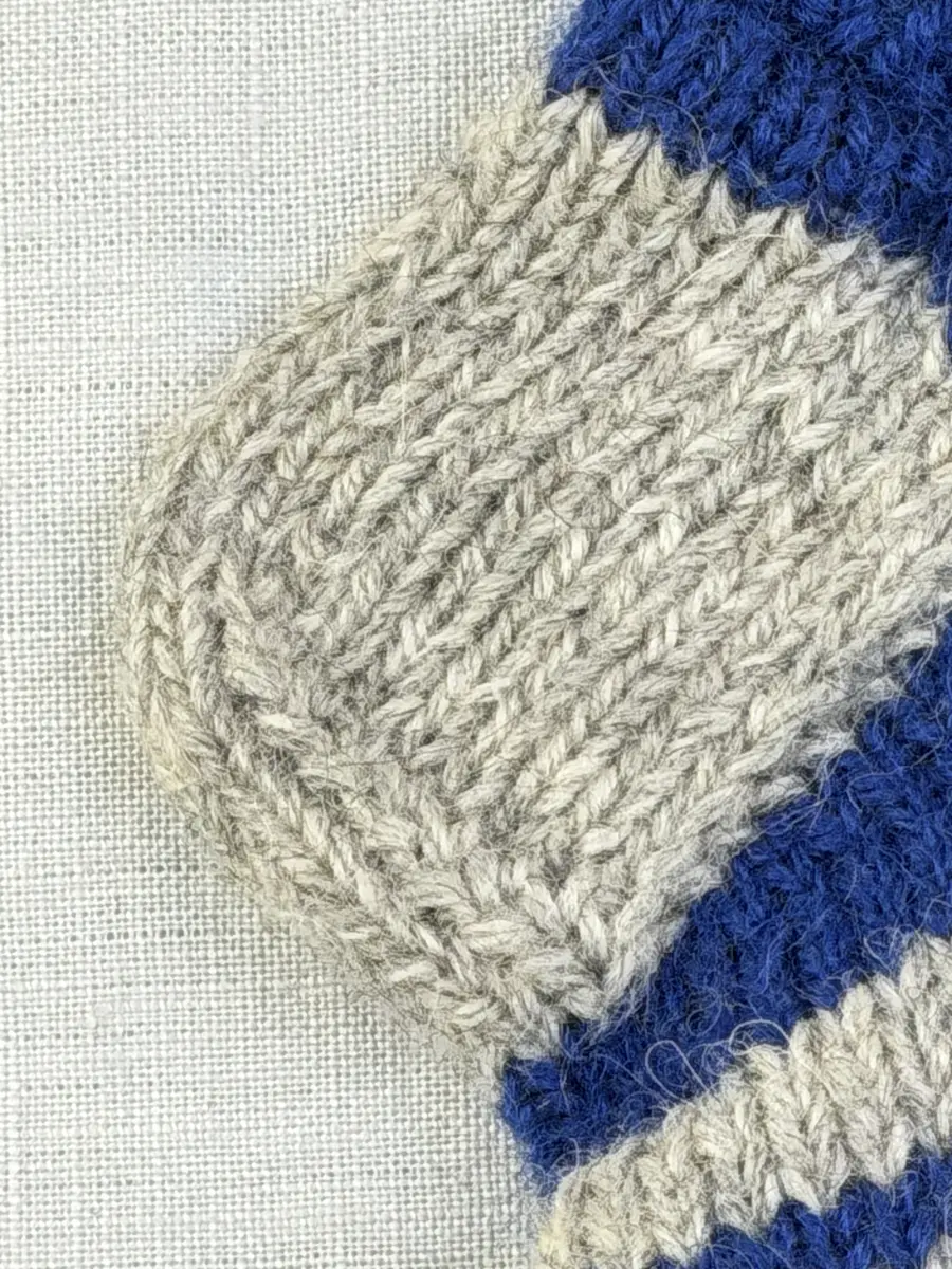 En stickad socka, med randig mudd i 1-1 resår (1 rät och 1 avig maska) och randig fot i slätstickning, av 3-trådigt Sportgarn i ull.
Gjord efter Bergå beskrivning D 315 från Bergå Färgeri & Ullspinneri, Stora Skedvi, Dalarna.