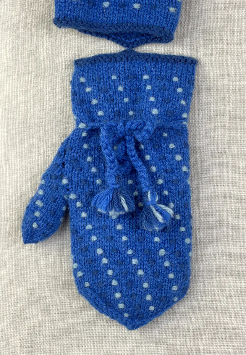 Ett par stickade damvantar, i slätstickning med nockor på vantens insida, av 3-trådigt sportgarn i ull. Nockornas/knutarnas "baksida" bildar ett prickmönster på vantens utsida. 
Vanten har två garntofsar med virkad snodd, kiltumme och är avslutad med bandhoptagning i toppen.