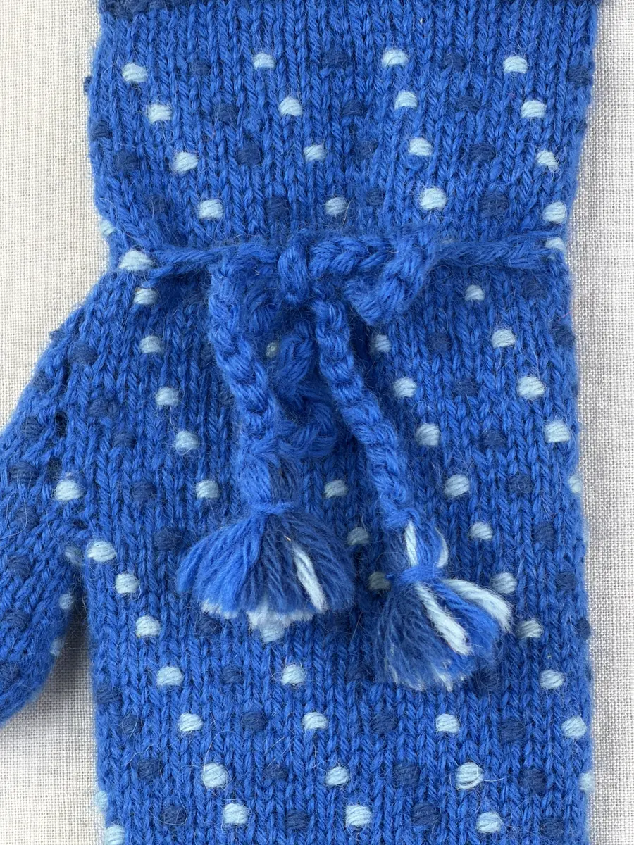 Ett par stickade damvantar, i slätstickning med nockor på vantens insida, av 3-trådigt sportgarn i ull. Nockornas/knutarnas "baksida" bildar ett prickmönster på vantens utsida. 
Vanten har två garntofsar med virkad snodd, kiltumme och är avslutad med bandhoptagning i toppen.