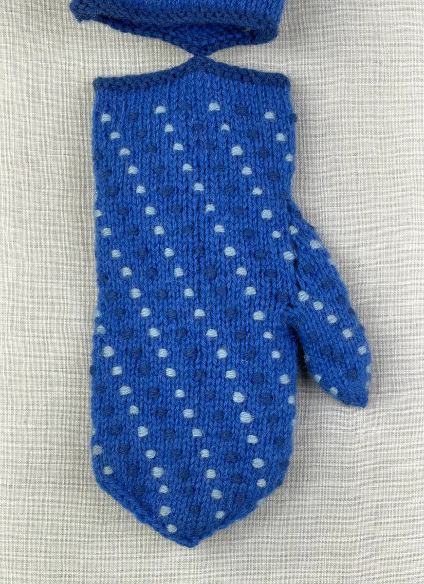 Ett par stickade damvantar, i slätstickning med nockor på vantens insida, av 3-trådigt sportgarn i ull. Nockornas/knutarnas "baksida" bildar ett prickmönster på vantens utsida. 
Vanten har två garntofsar med virkad snodd, kiltumme och är avslutad med bandhoptagning i toppen.