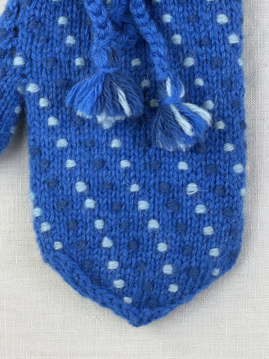 Ett par stickade damvantar, i slätstickning med nockor på vantens insida, av 3-trådigt sportgarn i ull. Nockornas/knutarnas "baksida" bildar ett prickmönster på vantens utsida. 
Vanten har två garntofsar med virkad snodd, kiltumme och är avslutad med bandhoptagning i toppen.