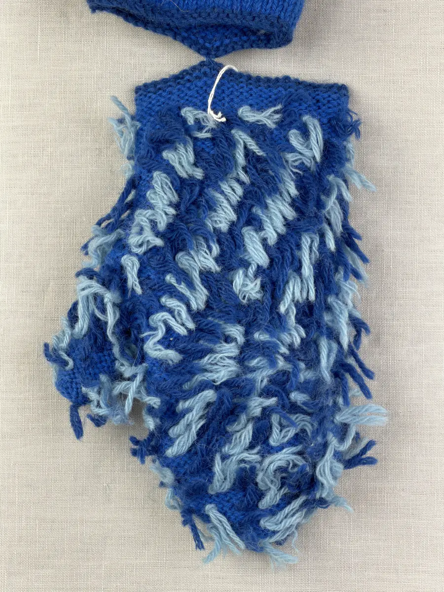 Ett par stickade damvantar, i slätstickning med nockor på vantens insida, av 3-trådigt sportgarn i ull. Nockornas/knutarnas "baksida" bildar ett prickmönster på vantens utsida. 
Vanten har två garntofsar med virkad snodd, kiltumme och är avslutad med bandhoptagning i toppen.