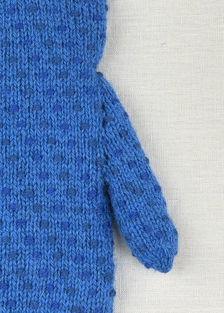 Ett par stickade herrvantar, i slätstickning med nockor på vantens insida, av 3-trådigt sportgarn i ull. Nockornas/knutarnas "baksida" bildar ett prickmönster på vantens utsida. 
Vanten har två garntofsar med virkad snodd, kiltumme i sidan och är avslutad med bandhoptagning i toppen.