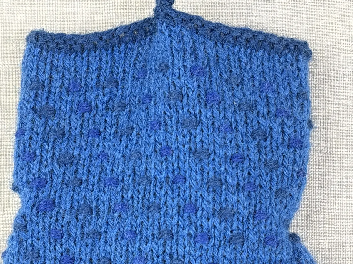 Ett par stickade herrvantar, i slätstickning med nockor på vantens insida, av 3-trådigt sportgarn i ull. Nockornas/knutarnas "baksida" bildar ett prickmönster på vantens utsida. 
Vanten har två garntofsar med virkad snodd, kiltumme i sidan och är avslutad med bandhoptagning i toppen.