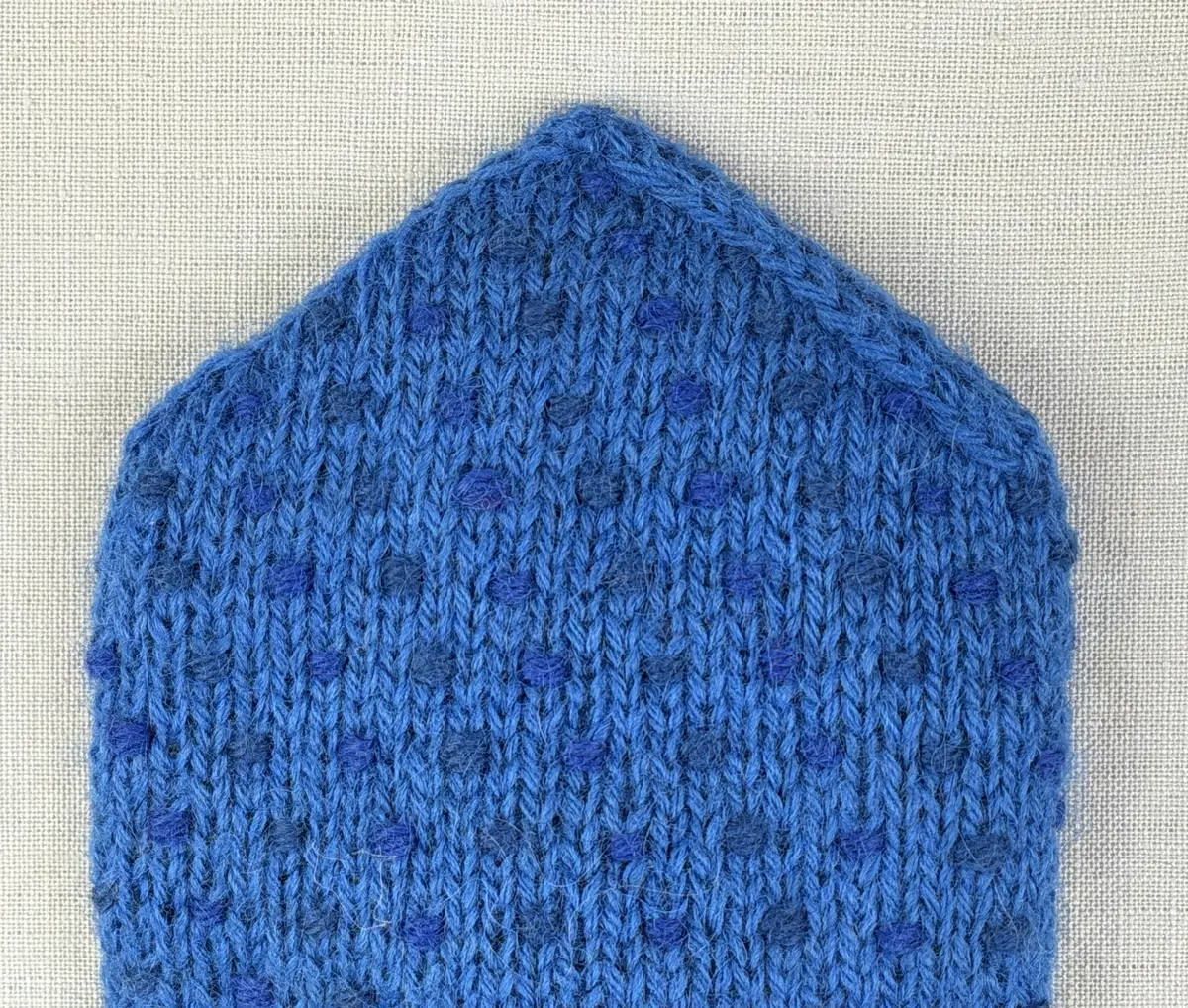 Ett par stickade herrvantar, i slätstickning med nockor på vantens insida, av 3-trådigt sportgarn i ull. Nockornas/knutarnas "baksida" bildar ett prickmönster på vantens utsida. 
Vanten har två garntofsar med virkad snodd, kiltumme i sidan och är avslutad med bandhoptagning i toppen.