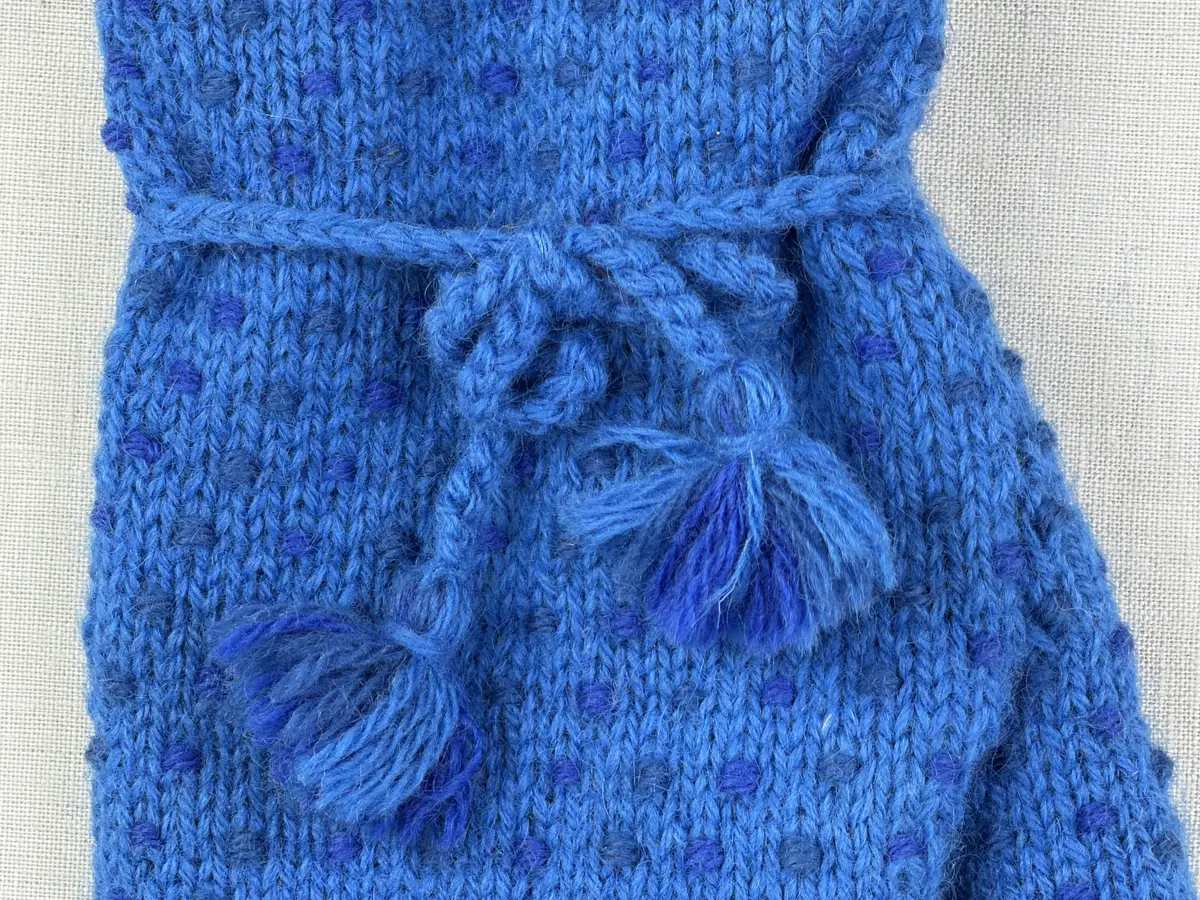 Ett par stickade herrvantar, i slätstickning med nockor på vantens insida, av 3-trådigt sportgarn i ull. Nockornas/knutarnas "baksida" bildar ett prickmönster på vantens utsida. 
Vanten har två garntofsar med virkad snodd, kiltumme i sidan och är avslutad med bandhoptagning i toppen.