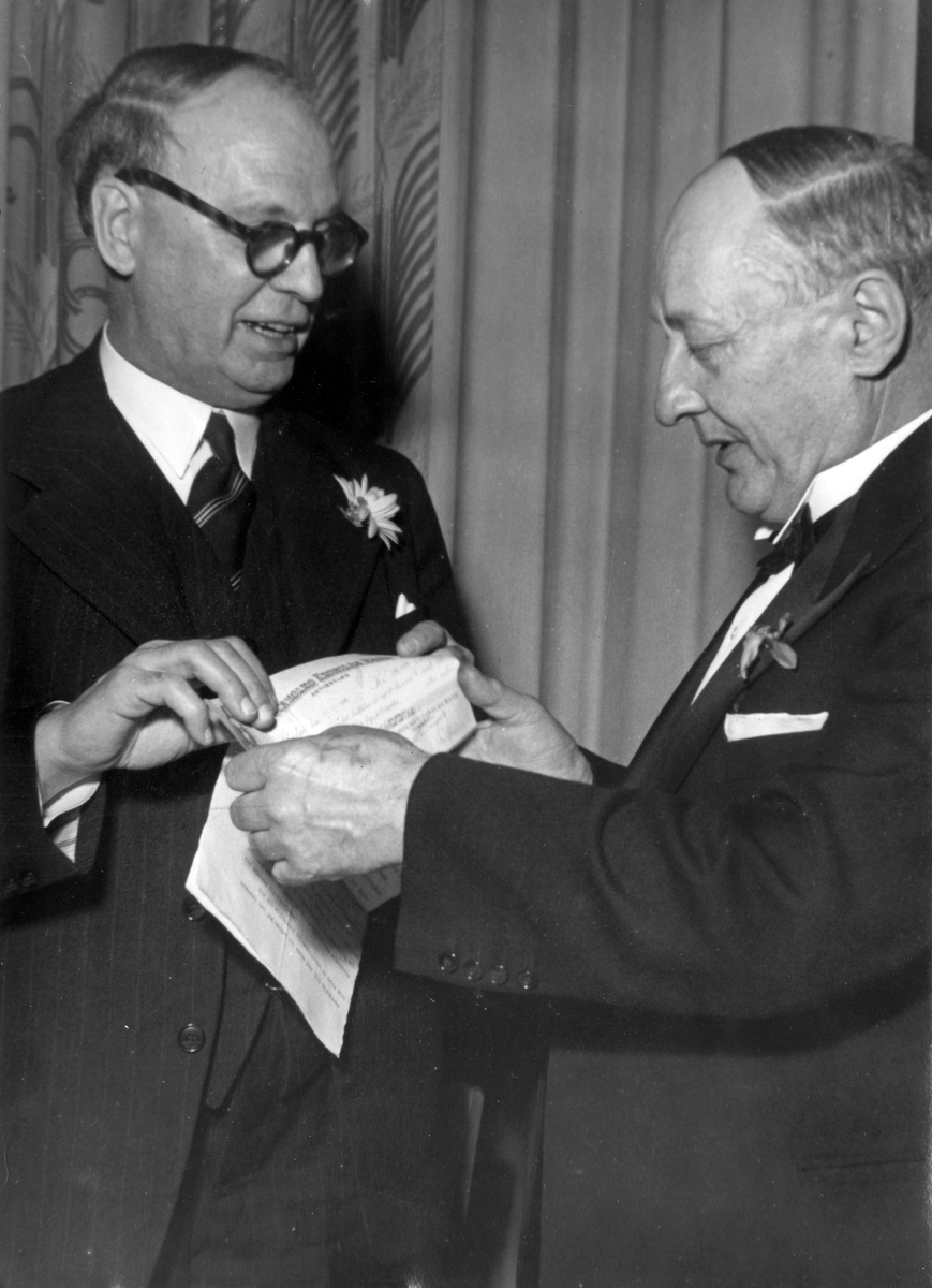 Nynäshamn blir stad. Festbanketten på Nynäs Hotell, nyårsafton 1945. Landshövding Levinsson delar ut Axel A-son Johnssons gåva på 100.000 kr till staden. Borgmästaren Albin Grönkvist tar emot gåvan å stadens vägnar. 

Historisk händelse, nyhet.

Personer på bilden:
Landshövdingen Levinsson och Albin Grönkvist.