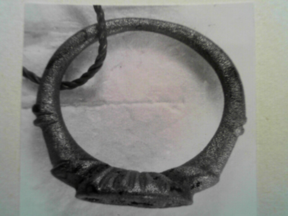 Messing. Tinn ?. Oval ring. Oval signetplate med utydelig mønster. Spor av rød lakk (?) i platen. Ryggen av platen har riller. Muligens overtrekk av tinn (?) på ringen.