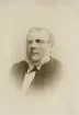 En äldre man i mörk kostym med väst.
Kronolänsman Johan Magnus Wilhelm Eksandh, Slätthög.
Bröstbild, halvprofil. Ateljéfoto.