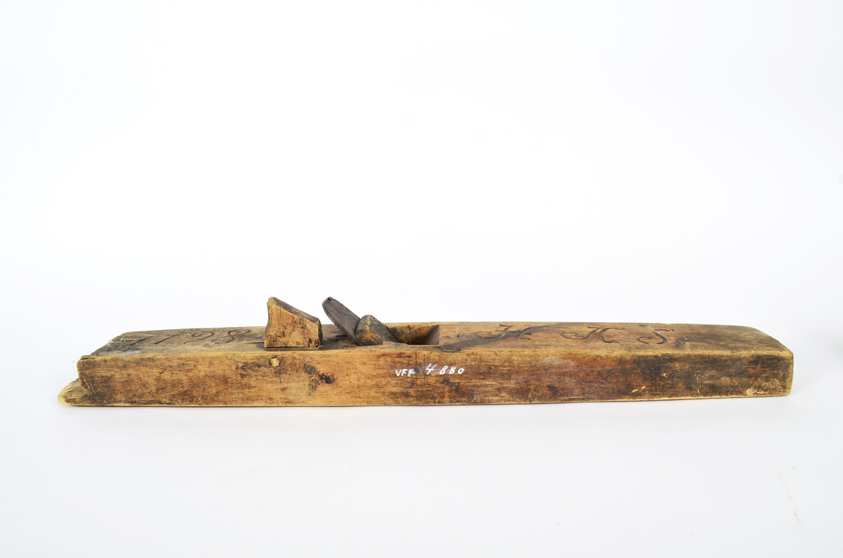 Sponhøvel i bjørk. Utskåren, lite utsprang nederst på bakre del. Nærmest rektangulært hull som smalner nedover med kniv og tretapp til festing, og rom til spon framom. Lite håndtak mot venstre side, lengre bak, festet med trenagle. Innskåret initialer og årstall.