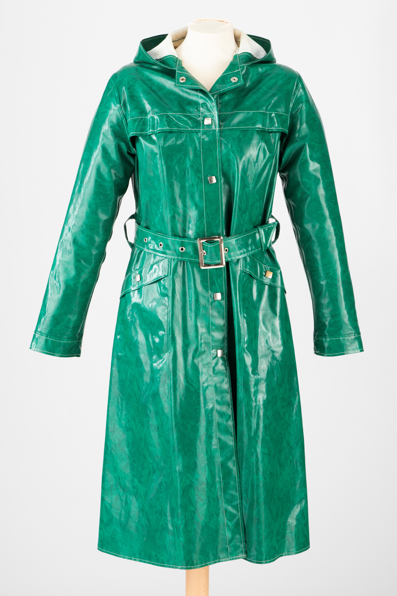 Innsvinget, midilang regnkåpe med hette. Dekorative, fritthengende "kapper" på hvert bryst og skråstilte stikklommer på hver hofte, lukket med fastsydd klaff med trykknapp. Midt bak er det en gåsplitt fra falden og helt opp til midjen, kneppet igjen med fire trykknapper øverst. Frakken er lukket midt foran med seks trykknapper, og midjen markert med et bredt belte med blank spenne og metallmaljer. Alle trykknappene er flate, firkantede og dekorative, av halvblankt, sølvfarget metall. Alle sømmer mellom stoffdelene er sveiset. Alle andre markert som hvite stikninger.