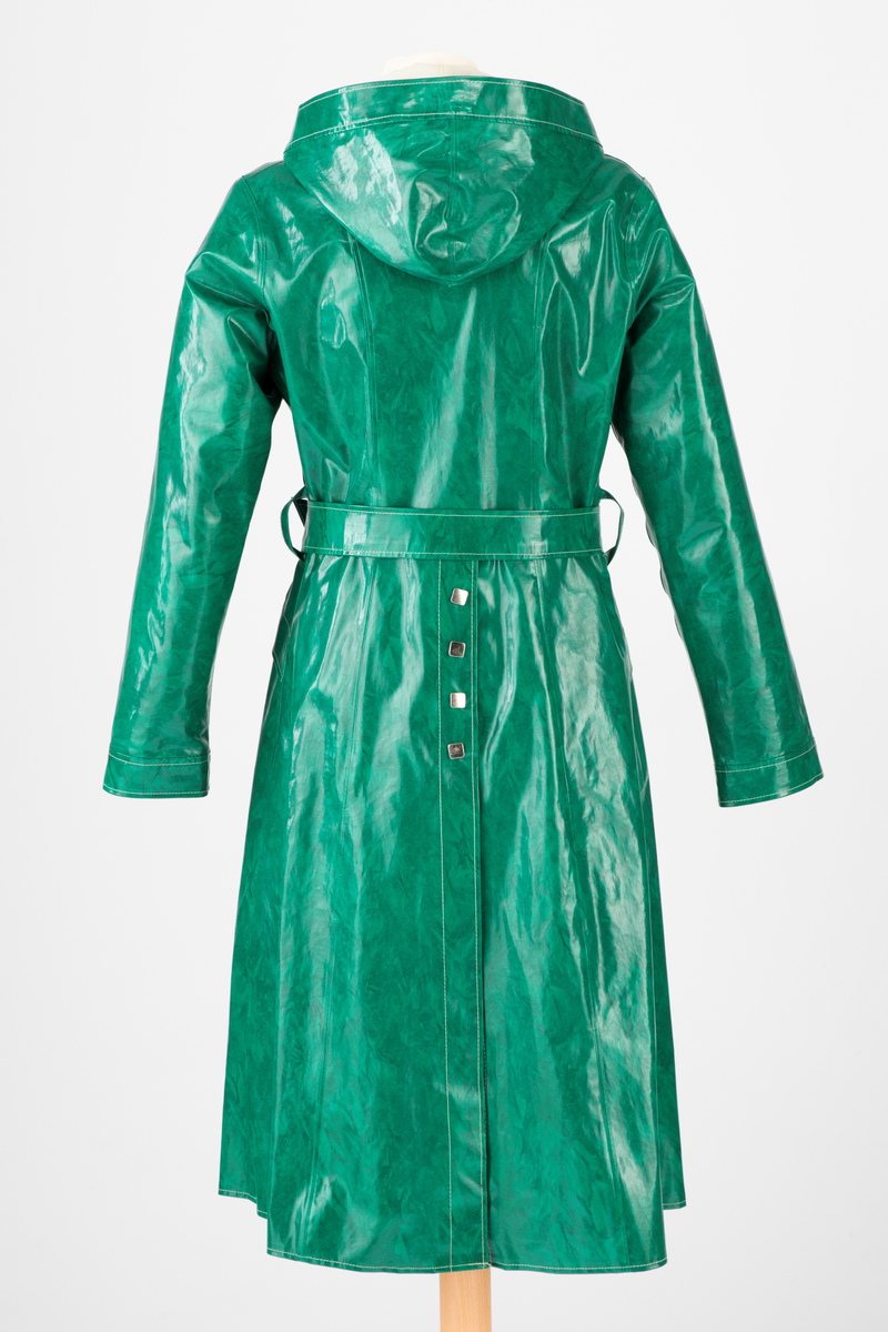 Innsvinget, midilang regnkåpe med hette. Dekorative, fritthengende "kapper" på hvert bryst og skråstilte stikklommer på hver hofte, lukket med fastsydd klaff med trykknapp. Midt bak er det en gåsplitt fra falden og helt opp til midjen, kneppet igjen med fire trykknapper øverst. Frakken er lukket midt foran med seks trykknapper, og midjen markert med et bredt belte med blank spenne og metallmaljer. Alle trykknappene er flate, firkantede og dekorative, av halvblankt, sølvfarget metall. Alle sømmer mellom stoffdelene er sveiset. Alle andre markert som hvite stikninger.