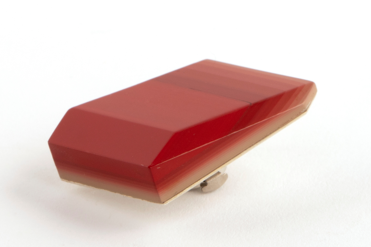 Brosje lagd av Urushi-lakk med teknikken cho-shitsu. 3 mm tykke lag lakt 100 ganger. Overgangen mellom lagene synes i fargene på lakken. Brosjen kan sies å være todelt. Nederste del kan sees som en base der fargene på lakklagene går fra lys gulbeige til mørk rød. Den øverste delen er monokrom rød. Brosjen har syv kanter og skaper en tredimensjonal effekt. Lakken er montert på en sølvplate med pin.