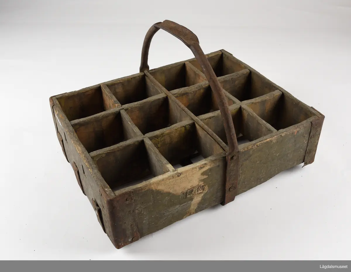 Trekasse med rom for tolv flasker. Jernhåndtak og jernbeslag i hjørnene og under. På langsiden er det brennmerket inn "MRIEF"