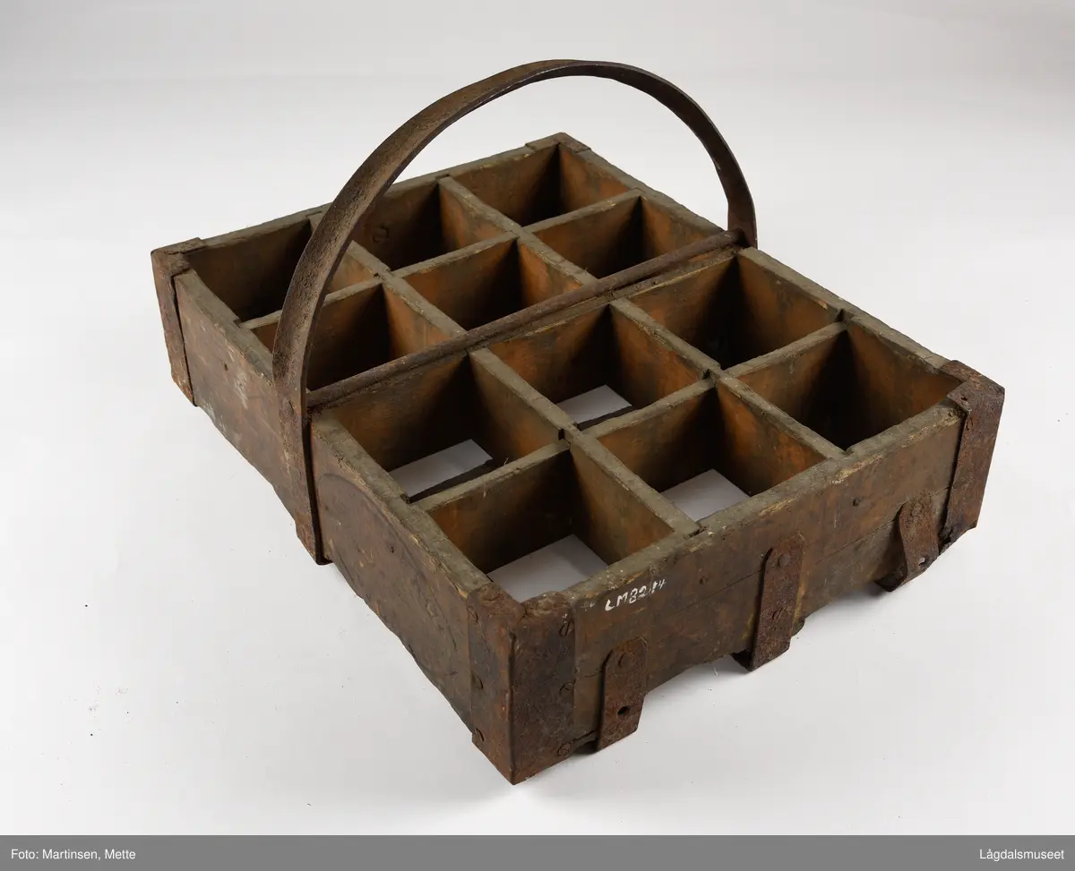 Trekasse med rom for tolv flasker. Jernhåndtak og jernbeslag i hjørnene og under. På begge langsidene er det brennmerket inn "KONGSBERG BRYGGERI"