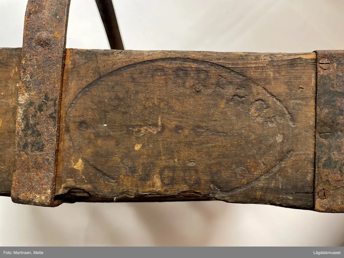 Trekasse med rom for tolv flasker. Jernhåndtak og jernbeslag i hjørnene og under. På begge langsidene er det brennmerket inn "KONGSBERG BRYGGERI"