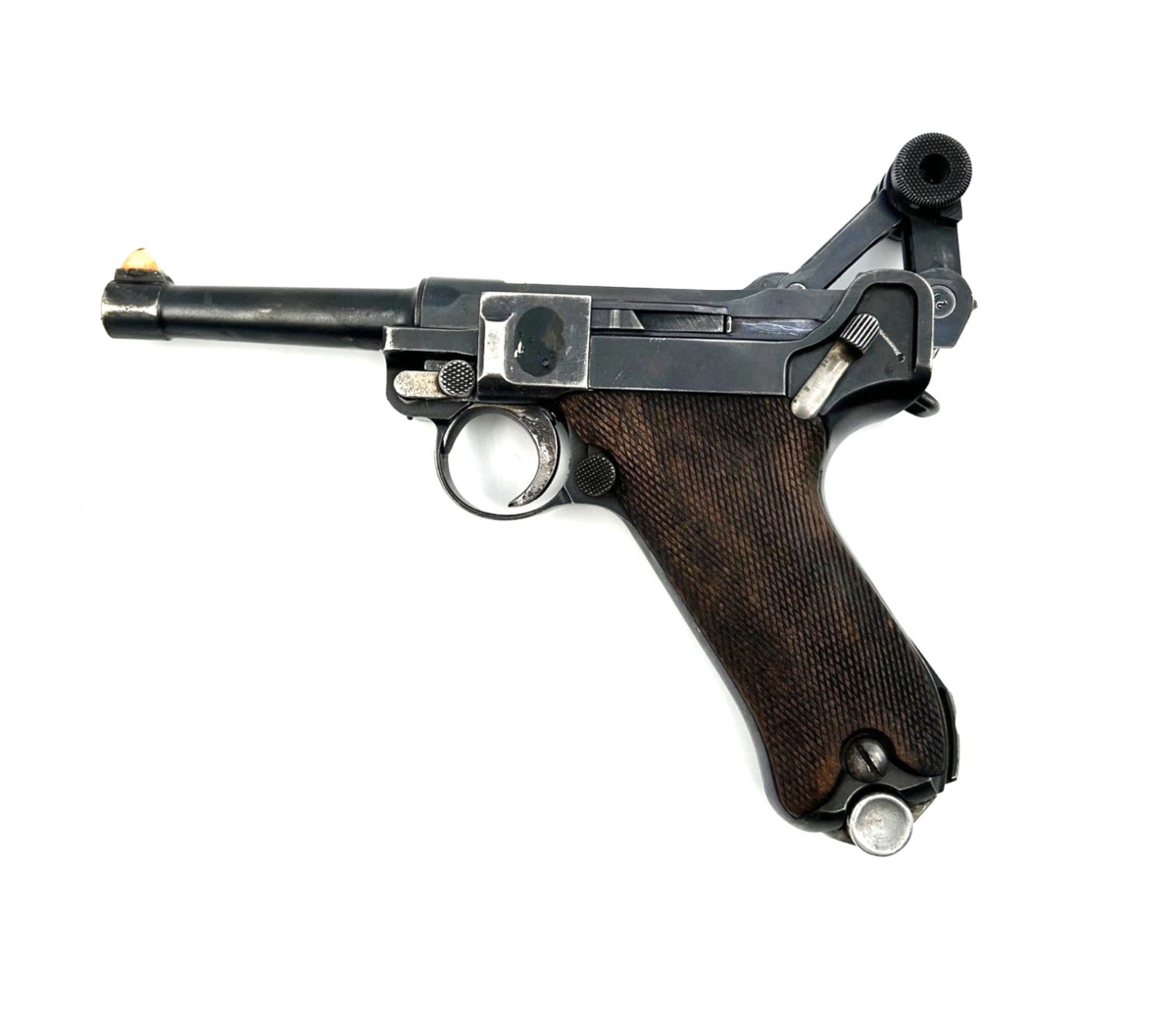 Pistol av modell Luger P08 Parabellum, automatpistol. Smal pipa samt grepp klätt av trä med nätmönster, så kallad nätskärning. Stommens sida samt pipans underdel stämplad med krönt "N". Stommens sida märkt "S/42" samt en mängd nummer 65, 43 samt 9570. Greppets baksida märkt: "M" ankare samt "N.122". Siktet är rödmålat som vittnar om vapnets användning inom skjutsport. Lackrest på stommens ena sida, troligen från ett tidigare fäst märke. Magasinet märkt: 9503, ett u i skrivstil samt stämpel av tyska örnen och nummer 63. Det finns en spricka i manteln.