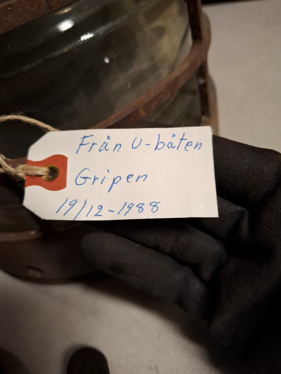 Lanterna i stål och glas. Cylinderformad. Lapp med texten: "Från u-båten Gripen 19/12-1988". Delar av glaset är krossat, väldigt rostig.
