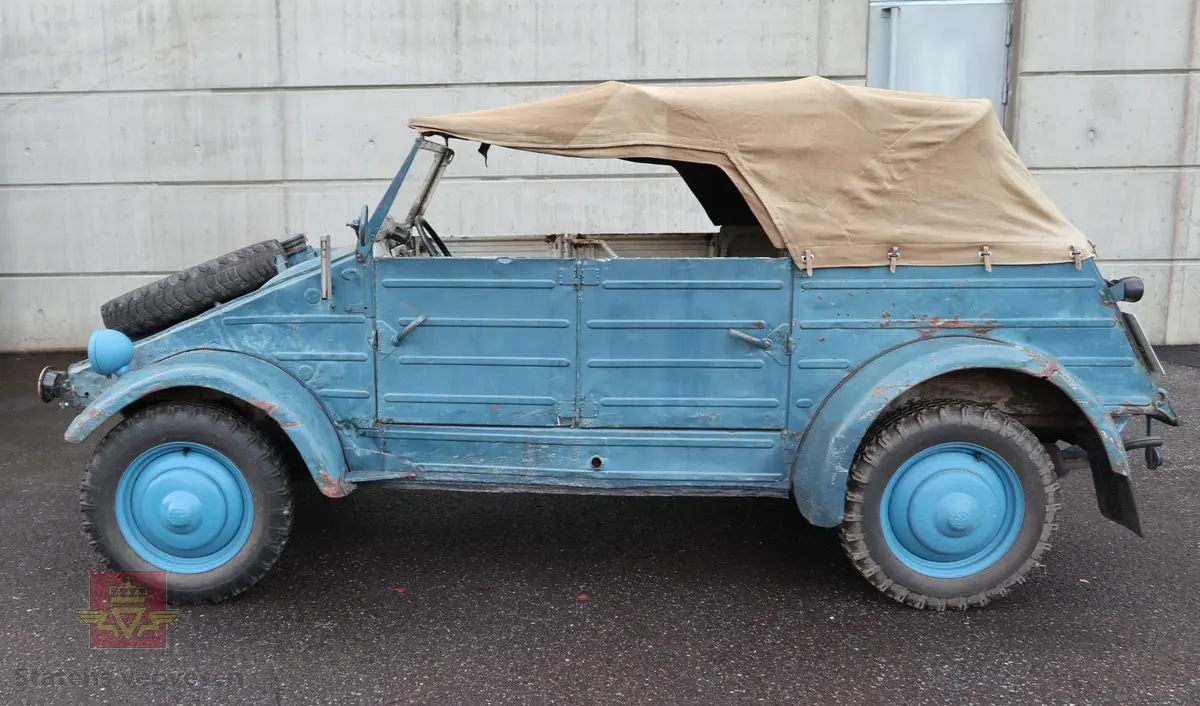 Volkswagen Typ 82 Kübelwagen. Åpen (med kalesje). Blå utvendig og hvit innvendig. Opprinnelig har hele bilen vært sandfarget. Man kan også se rester av grønn farge under det blå. Svart motorrom. Bilen har fire hjul og er toakslet med trekk på bakre. Bensindrevet firesylindret firetakts motor med et sylindervolum på 1192 cm3 og en effekt på 31 hk - 23 kW. Motoren har forgasser, er luftavkjølt, og sitter bak på bilen. 4-trinns manuell girkasse med spak i gulvet. Antall sitteplasser var tre ettersom dette opprinnelig er en radiobil, men nå har bilen sofa bak som tilsier fire sitteplasser totalt. Original dekkdimensjon rundt om skal være 5.00 x 16. Bilen har innvendig gulv av tre, dette er ikke det originale. Frontruta er sprekt. Kilometerstand på instrumentet viser 28084 km.