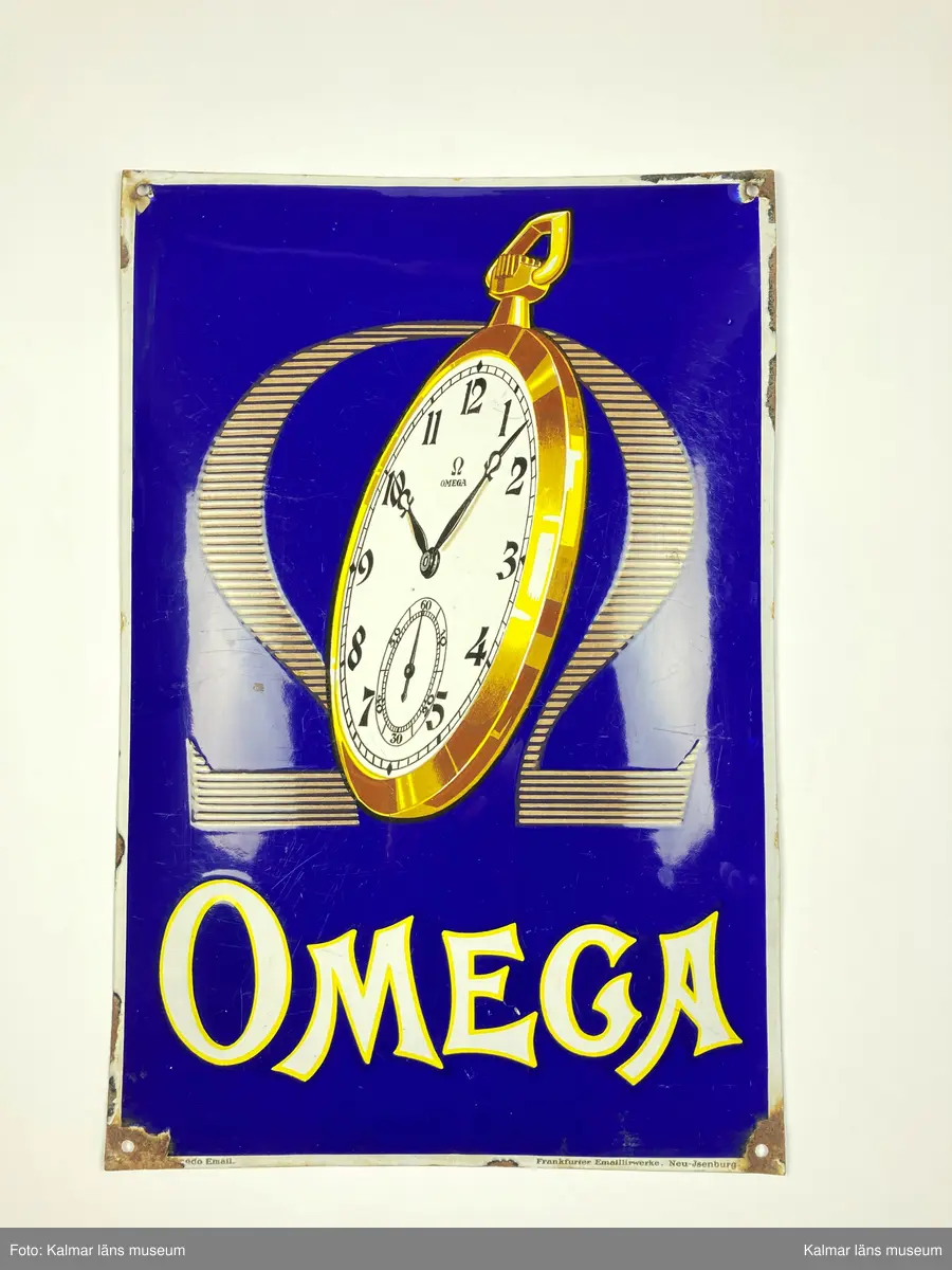 KLM 24993:170. Skylt. Rektangulär och något kupad skylt i emaljerad metall. Blå bakgrund med motiv i gult och vitt föreställande ett fickur och omegatecken samt texten OMEGA. I nedre högra hörnet text: Frankfurter Emaillirwerke, Neu-Jsenburg.