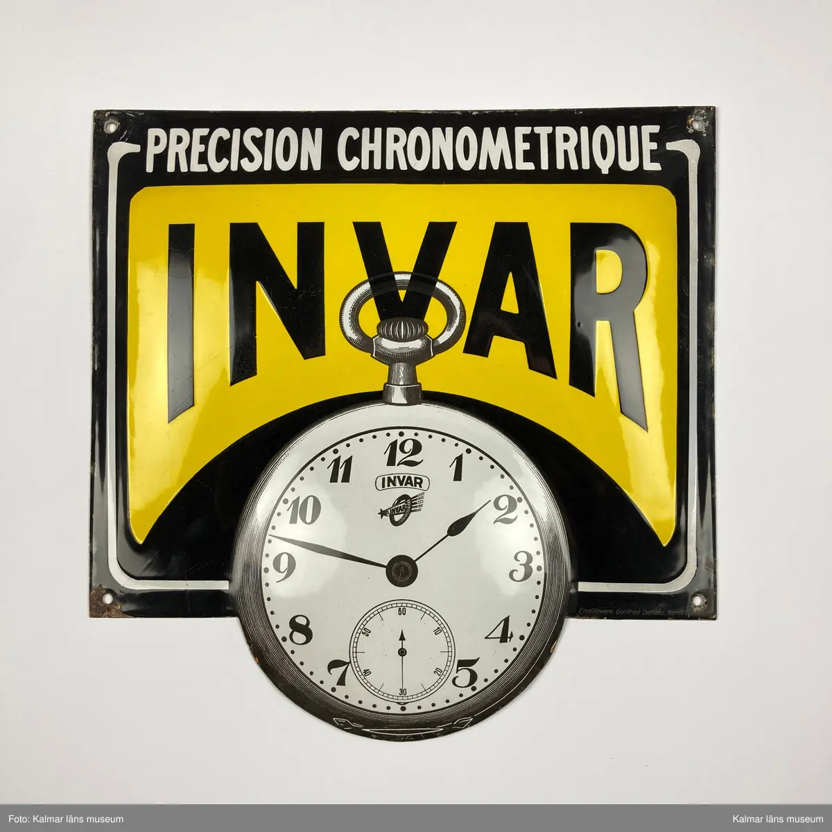 KLM 24993:171. Skylt. Liggande rektangulär och något kupad skylt av emaljerad metall. Svart och gul bakgrund med detaljer i vitt, text: PRECISION CRONOMETRIQUE INVAR. Nedre delen av skylten i form av ett fickur. I nedre högra hörnet text: Emaillirwerk Gottfried Dichanz Berlin.