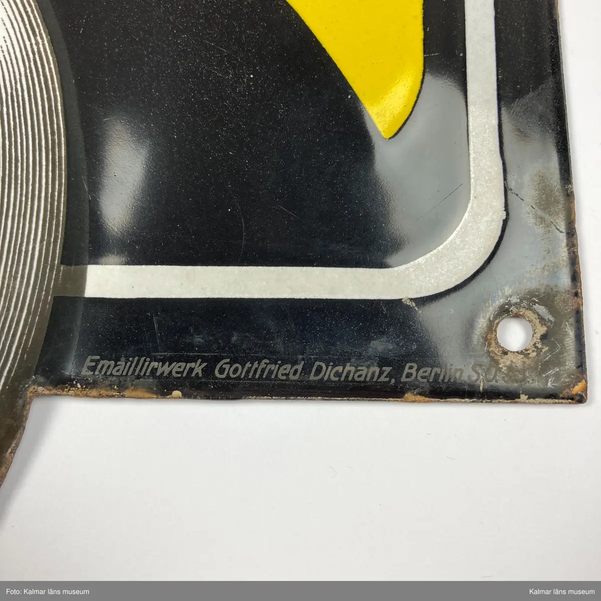 KLM 24993:171. Skylt. Liggande rektangulär och något kupad skylt av emaljerad metall. Svart och gul bakgrund med detaljer i vitt, text: PRECISION CRONOMETRIQUE INVAR. Nedre delen av skylten i form av ett fickur. I nedre högra hörnet text: Emaillirwerk Gottfried Dichanz Berlin.