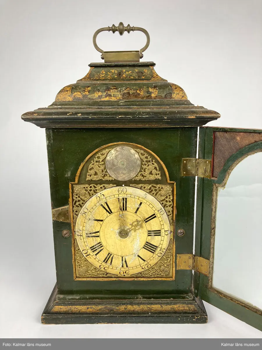 KLM 2269. Bordsur. Fodral av trä, lackerat i grönt med målade kinesiska figurer och landskap i svart och guld. Upptill handtag av mässing. Samtliga sidor är försedda med glaspartier och upptill mindre rutor med spegelglas. Både baksida och framsida kan öppnas. Vitmålad urtavla omgiven av bronsornament. Urverket av mässing och stål med rik ornering. Urverket är signerat: Hans Strehl 1637. Fodralet saknar fötter samt knoppar som suttit på ovansidan.